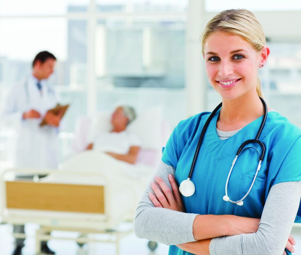 Young smiling doctor standing in hospital with colleagues talking to patient in background